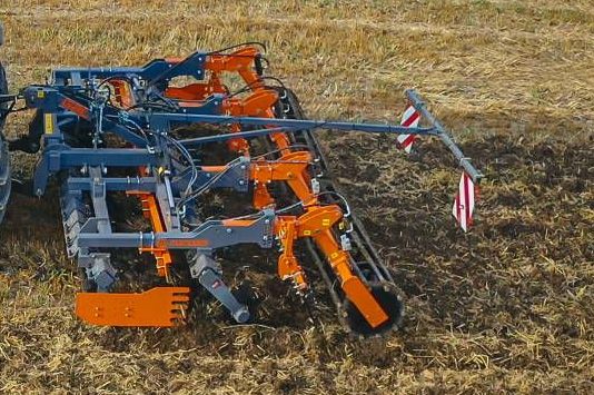 Déchaumeur à dents MANDAM bleu et orange en action, attelé à un tracteur pour la préparation du sol.