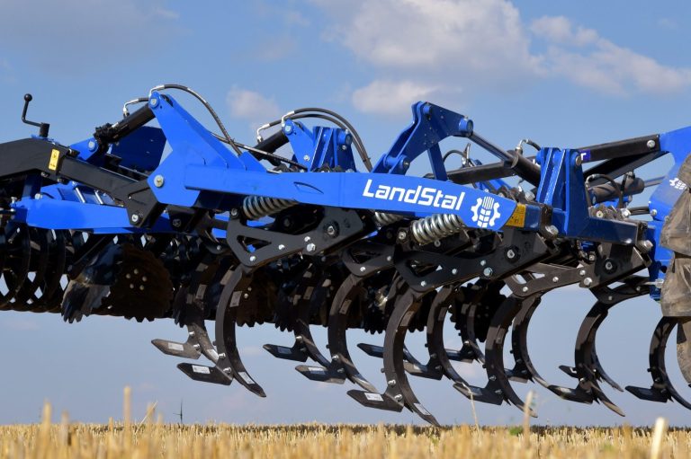 Déchaumeur à dents bleu et noir Landstal équipé de rouleaux de plombage à l'arrière.