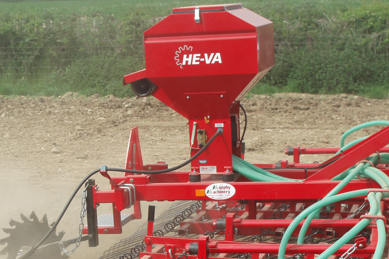 Trémie rouge He-Va au travail dans un champ pour semer de petites graines simultanément avec le travail du sol.