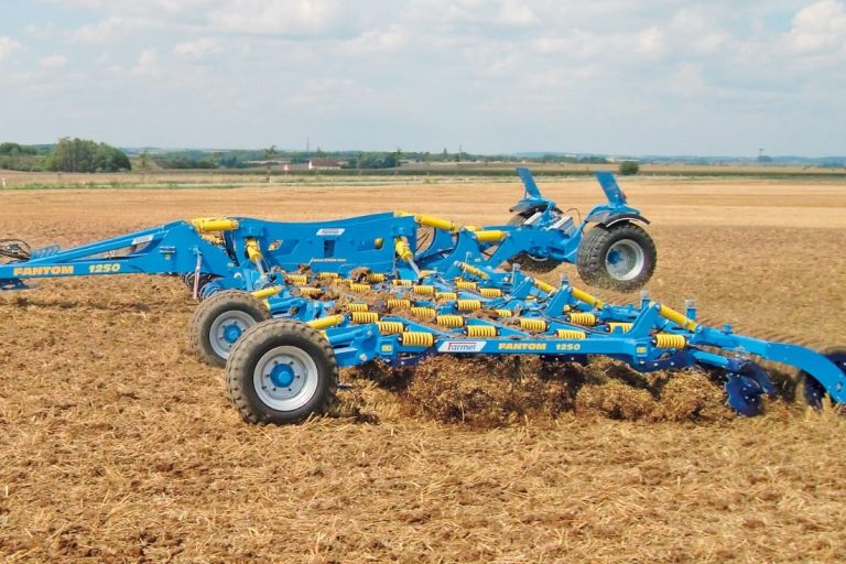 Cultivateur et déchaumeur à dents bleu FARMET au travail dans un champ pour un mélange homogène du sol.