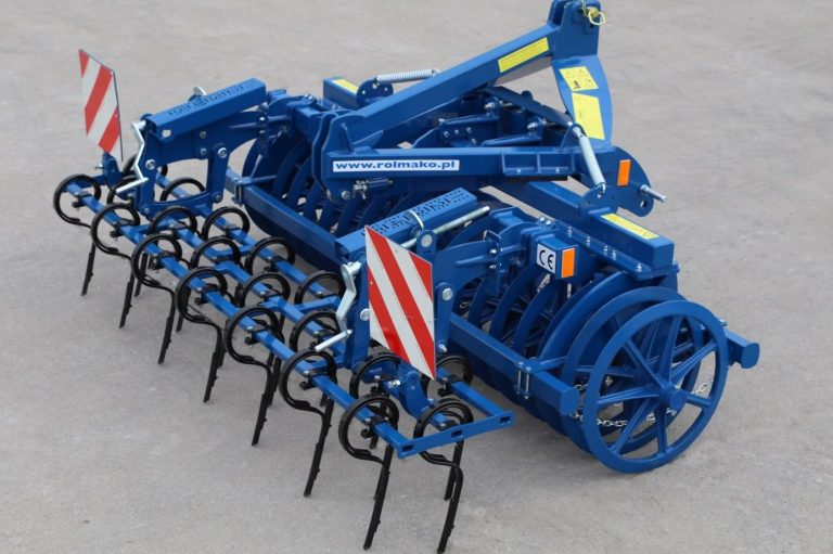 Outil frontal bleu Rolmako équipé de dents vibrantes et d'un rouleau, stationné dans la cour.