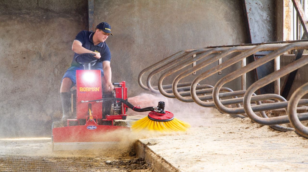 Nettoyeur de logettes Bobman elevage Éleveur utilisant un nettoyeur de logettes Bobman rouge avec brosse rotative jaune pour un entretien rapide et sans effort de l'étable.