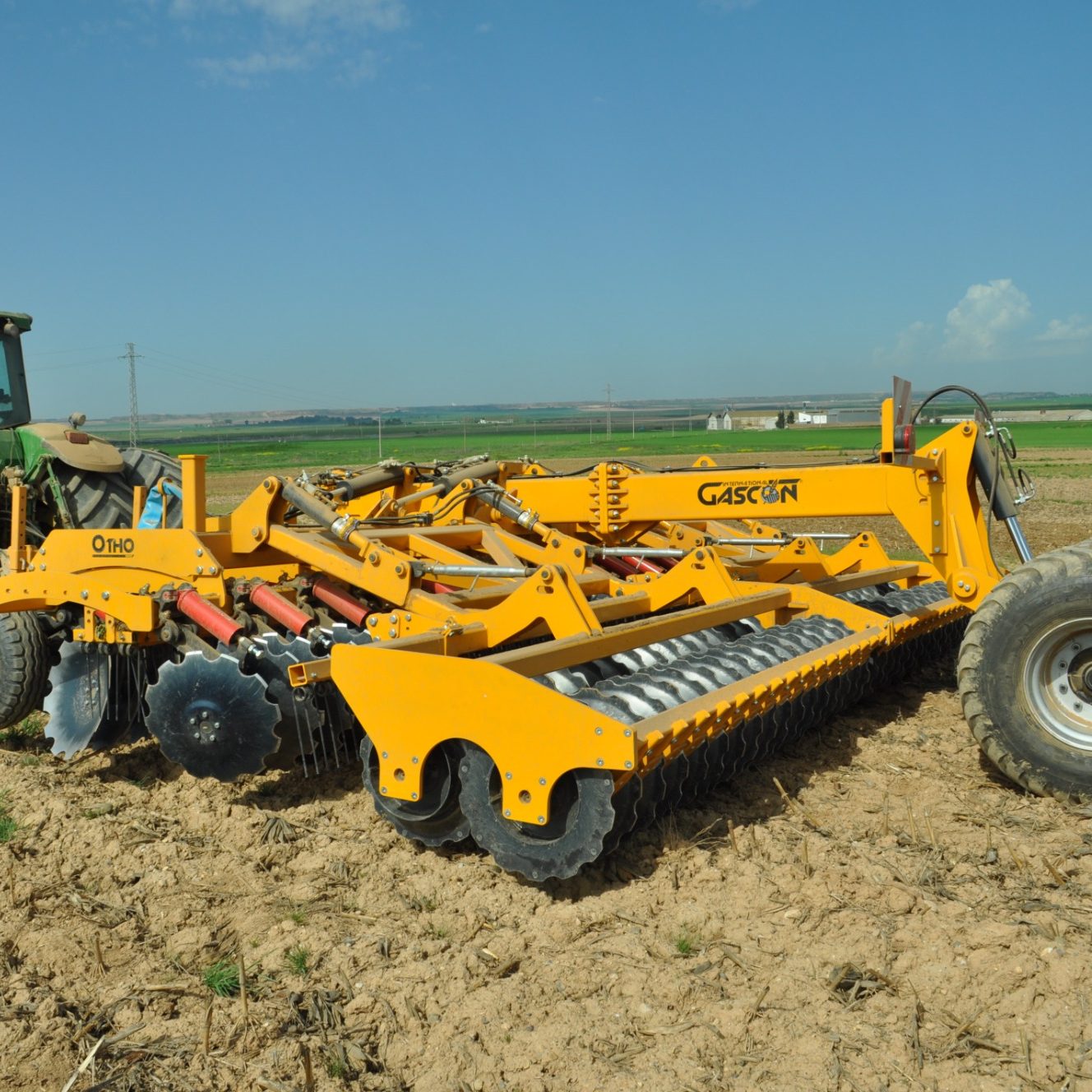 Grand outil de travail du sol jaune Gascon attelé à un tracteur, conçu pour une efficacité pure sur les terrains les plus durs.