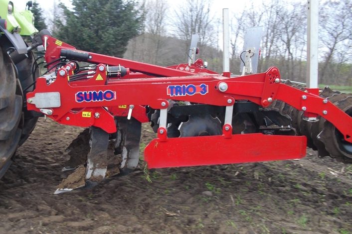 Décompacteur rouge de la marque Brix attelé à un tracteur pour un travail profond des sols compactés.