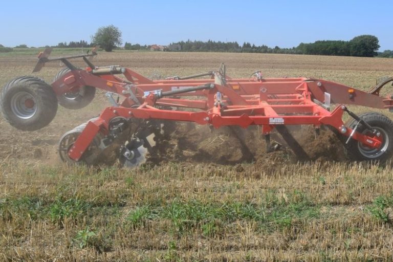 Cultivateur à dents rouge SMS Agro attelé à un tracteur, préparant le terrain.