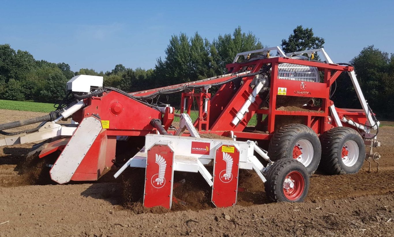 Ramasseuse à pierres Husarya rouge et blanche en pleine action pour assainir les sols et sécuriser les passages de machines.