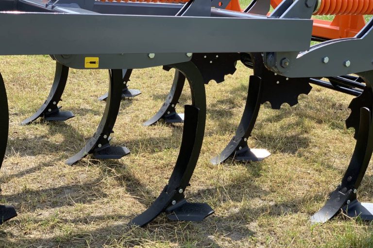 Détail des dents profilées d'un déchaumeur Mandam gris et noir posé sur un sol sec.