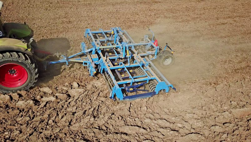 Préparateur de lit de semence bleu Farmet Kompaktomat au travail, réalisant 7 opérations agronomiques en un seul passage.