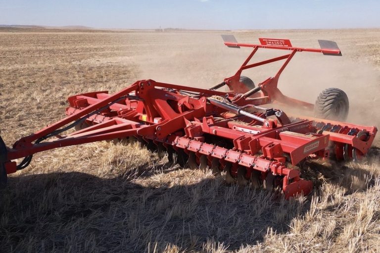 Déchaumeur rouge TOSCANO en action dans un champ cultivé, attelé à un tracteur agricole.