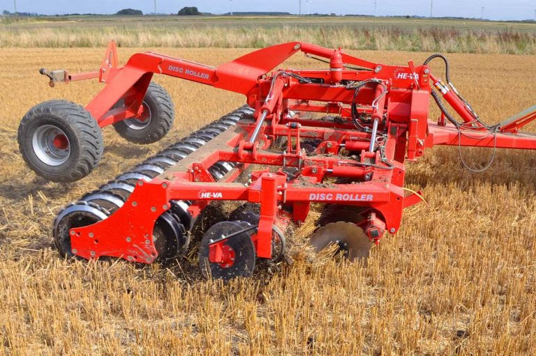 Grand déchaumeur à disques rouge HE-VA avec rouleau packer au travail dans un champ de chaume.
