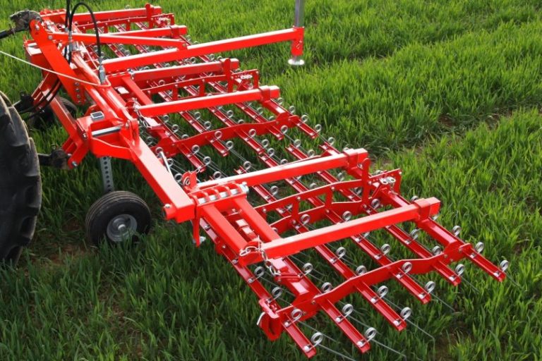 Herse étrille rouge de la marque SMS Agro posée sur l'herbe, prête pour vos chantiers de désherbage mécanique.