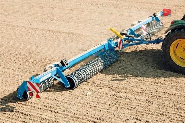 Rouleau agricole bleu Farmet attelé à un tracteur pour finaliser la préparation du lit de semence.