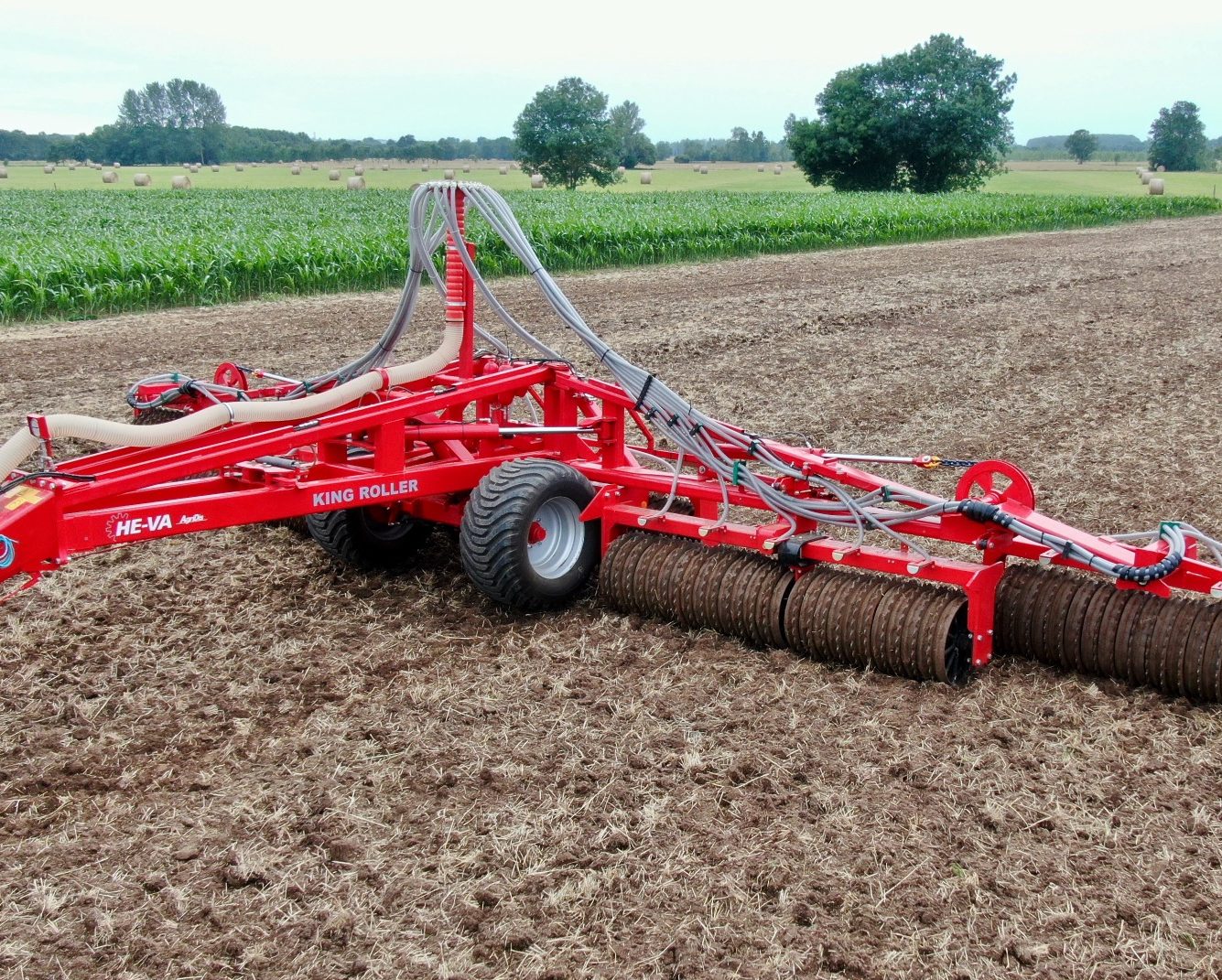 Large rouleau agricole rouge He-Va en action pour un émiettage parfait et une consolidation homogène du sol.