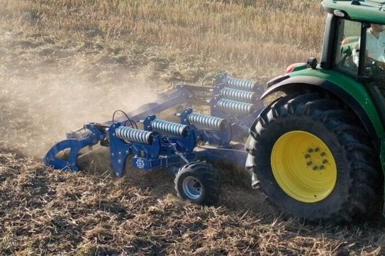 Tracteur attelé à un décompacteur bleu Landstal travaillant la terre pour éliminer les semelles de labour.