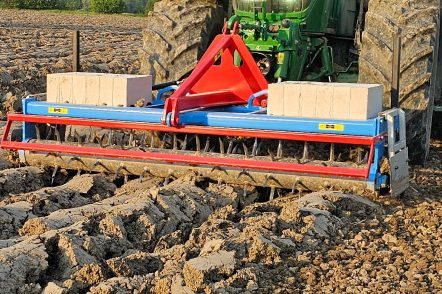 Outil frontal bleu et rouge Heilers lesté avec des masses, écrasant efficacement les mottes sur un labour.