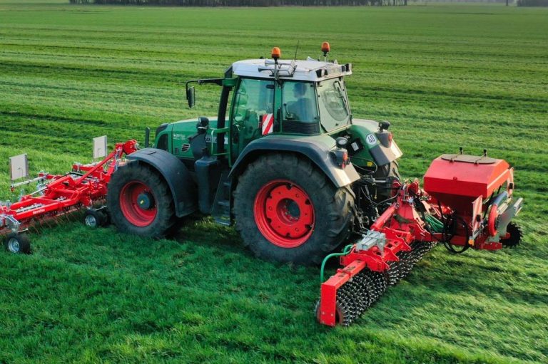 Outil rouge Guttler attelé à un tracteur en plein champ pour l'entretien des prairies, permettant d'émousser et d'aérer en un seul passage.