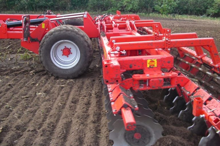 Grand déchaumeur rouge BRIX au travail dans un champ de sol labouré, montrant les disques.